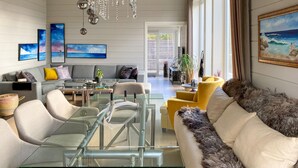 Ein modernes Wohnzimmer mit einem Glastisch, einer Couch, einem gelben Sessel und einem Gemälde, das eine Strandlandschaft zeigt.
