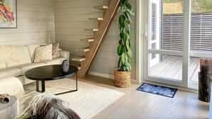 Ein modernes Wohnzimmer mit Sofa, Couchtisch, Treppe, Topfpflanze und Blick durch eine Glastür.