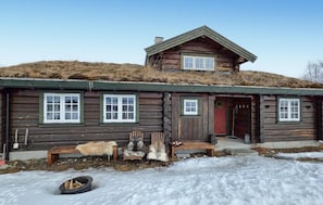 A log cabin with a front porch, a chimney, and a small garden area with a bench and a birdhouse.