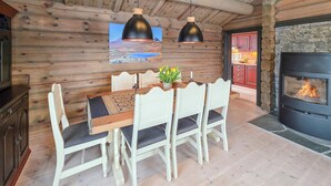A wooden interior with a dining table, chairs, pendant lights, a fireplace, and a kitchen area. - Amazing home in Ustaoset (Ustaoset)