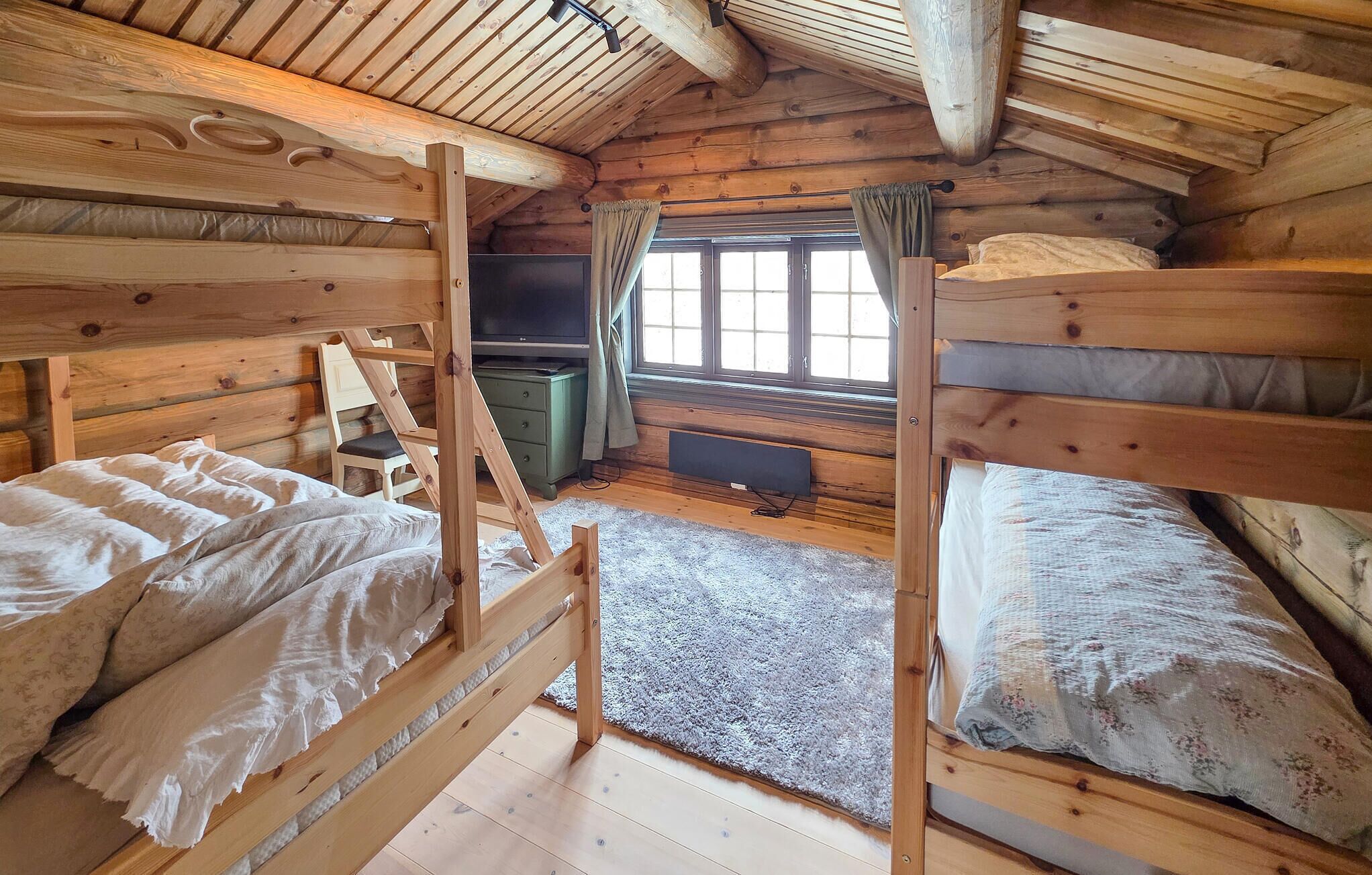 A cabin with two bunk beds, a desk, a television, and a window with curtains.
