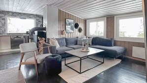 Un salon moderne avec un canapé d’angle gris, une table basse et un coin repas équipé d’une cuisinière.