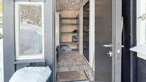 Un couloir étroit avec un banc, une porte et des étagères remplies d’objets.