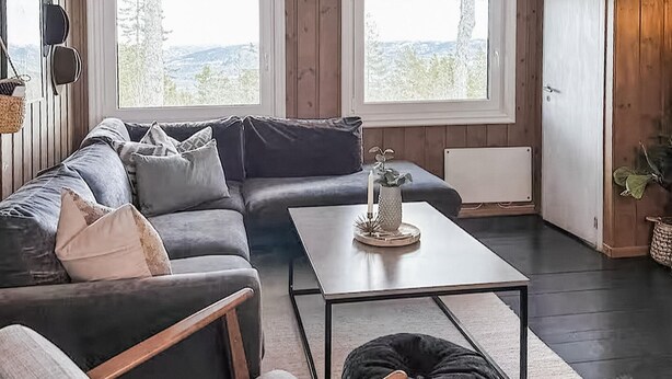 Un salon moderne avec un canapé d’angle, une table basse et une vue sur l’extérieur grâce à de grandes fenêtres.