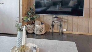 Une pièce dotée d’un grand téléviseur à écran plat, d’une petite table ronde, d’une plante en pot et d’un vase décoratif.