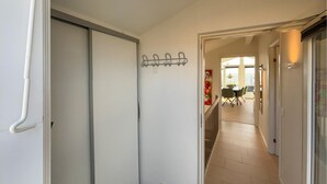Een gang die uitkomt in een eetgedeelte, met een kapstok, een eettafel met stoelen en een raam met jaloezieën.