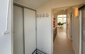 A hallway leading to a dining area with a coat rack, a dining table with chairs, and a window with blinds.