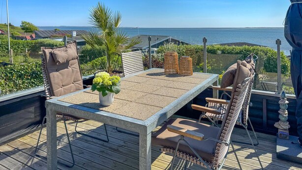 Een terras met een tafel en stoelen, een bloempot en uitzicht op zee.