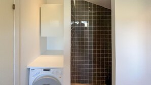 Een wasserette met een wasmachine, een betegelde muur en een deur naar een andere ruimte.