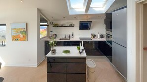 Een moderne keuken met een centraal eiland, zwarte kastjes, een ingebouwde oven en een dakraam.