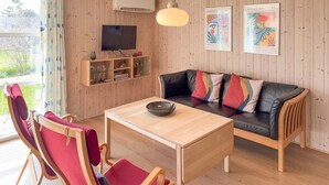 Olohuone, jossa on puuseinä, musta nahkasohva, puinen pöytä ja televisio.
