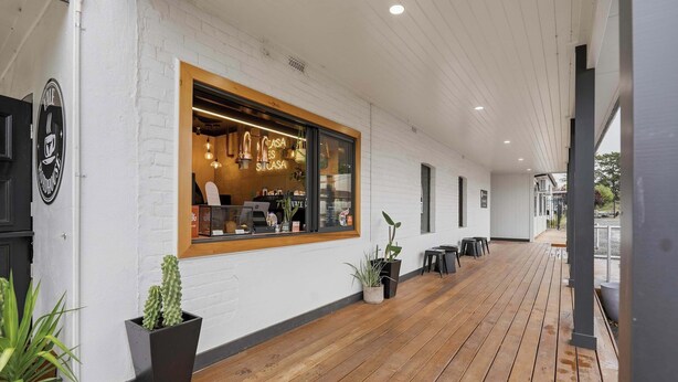 Una cafetería con terraza de madera, paredes de ladrillo blanco y plantas en macetas.