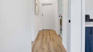 Un corridoio con pavimento in legno, pareti bianche e una porta in fondo.