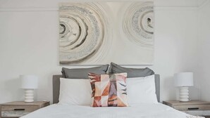 Un letto rifatto con cura, decorato da una coperta a motivi, due comodini con lampade e un'opera d'arte astratta sulla parete sopra il letto.