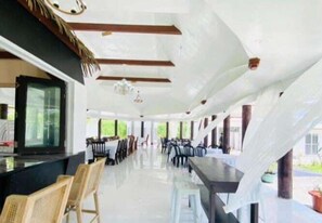 A spacious indoor area with a long counter, multiple tables, and chairs, likely a dining or meeting area. - Maota Hotel (Apia)