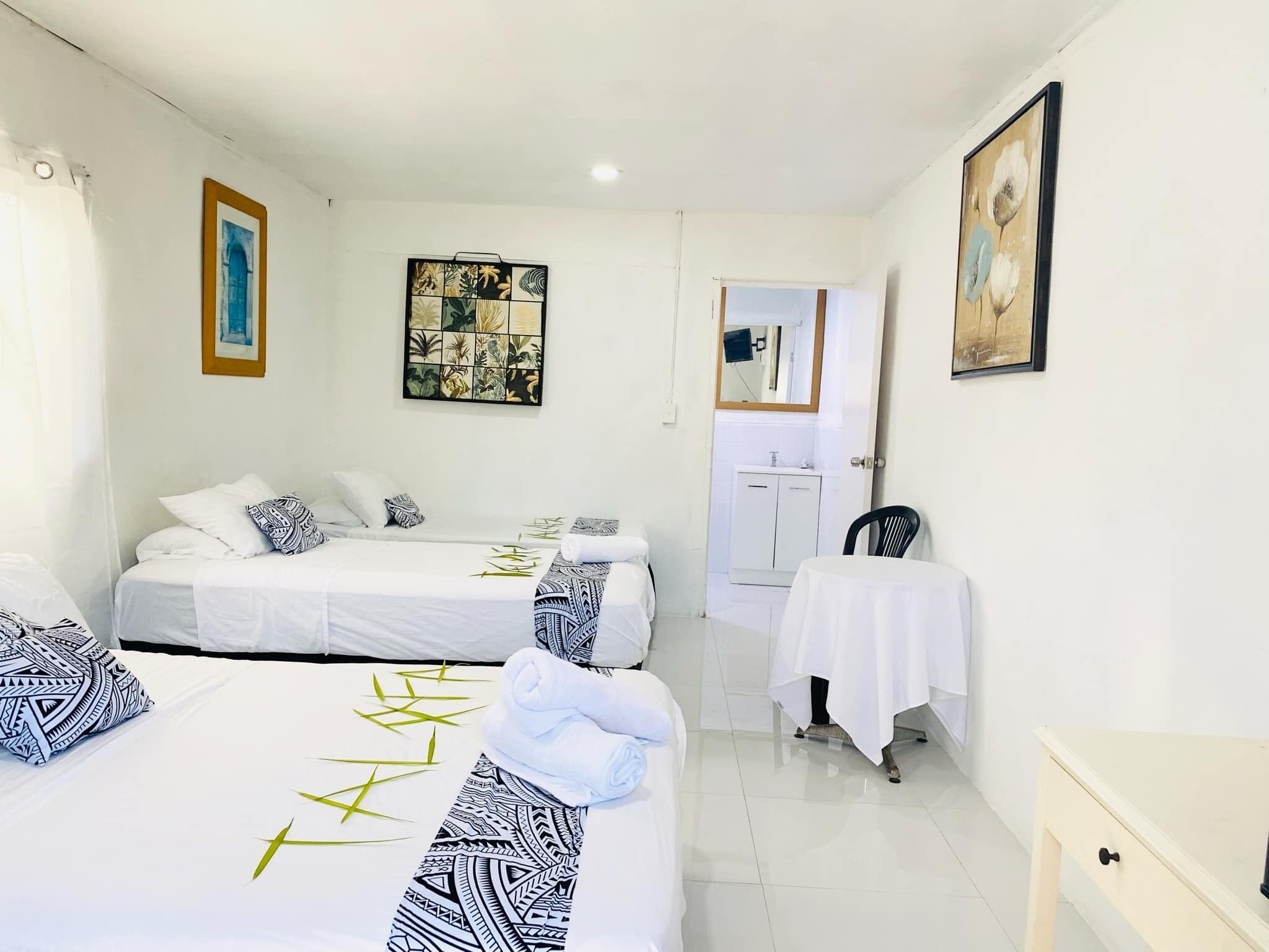 A hotel room with two beds, a small table, a chair, a bathroom, and artwork on the walls.