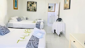 A hotel room with two beds, a small table, a chair, a bathroom, and artwork on the walls. - Maota Hotel (Apia)