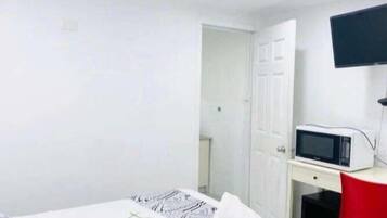 Una habitación con cama, escritorio, silla, televisor y puerta.