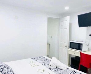 A room with a bed, a desk, a chair, a television, and a door. - Maota Hotel (Apia)