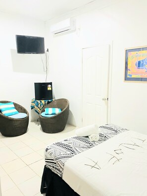 A room with a bed, two wicker chairs with cushions, a television mounted on the wall, and a door. - Maota Hotel (Apia)