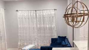 Un salon moderne comprenant un canapé, une petite table, un tapis à motifs et un coin cuisine doté d’un plan de travail en marbre.