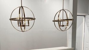 Une cuisine avec des meubles blancs, un plan de travail en marbre et deux luminaires suspendus.