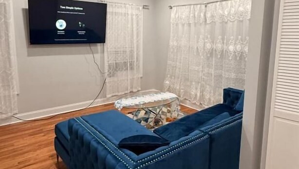 Un salon avec un canapé bleu, une table basse en verre, un téléviseur fixé au mur et un ventilateur de plafond.