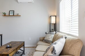 Ein Wohnzimmer mit einer Couch, einem Couchtisch, einer Stehlampe und einem Fenster mit Jalousien.