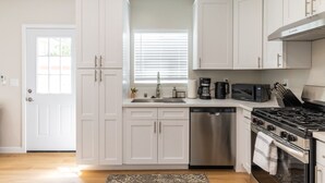 Una cucina con mobili bianchi, lavastoviglie, fornello e forno a microonde.