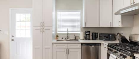 A modern kitchen with white cabinetry, stainless steel appliances, and a window with blinds.