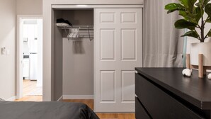 Una camera da letto con un letto, una cassettiera, un armadio pieno di vestiti e una pianta in vaso.