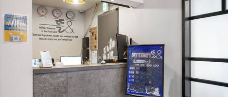 A hotel reception area with a counter, a digital display board, clocks, and a wall with text and images.