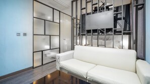 A modern living room with a white sofa, a glass partition, and a mounted television. - Design Hotel Tteulaen (Pyeongtaek)