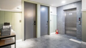 An elevator area with a fire extinguisher, a table with a basket, and a wall-mounted light. - Design Hotel Tteulaen (Pyeongtaek)