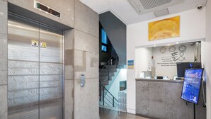 A hotel reception area with a modern design, including a reception desk, a digital screen, and a staircase. - Design Hotel Tteulaen (Pyeongtaek)