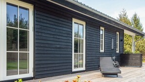 A modern house with a dark exterior, large windows, a wooden deck, outdoor seating, and potted plants. - 5 Star Holiday Home in Brovst (Brovst)