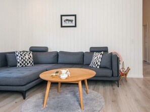 Una sala moderna con un sofá modular gris, una mesa de centro redonda de madera y una alfombra gris.