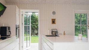 A modern kitchen with white cabinetry, a built-in stove, a coffee maker, and a large window. - 5 Star Holiday Home in Brovst (Brovst)