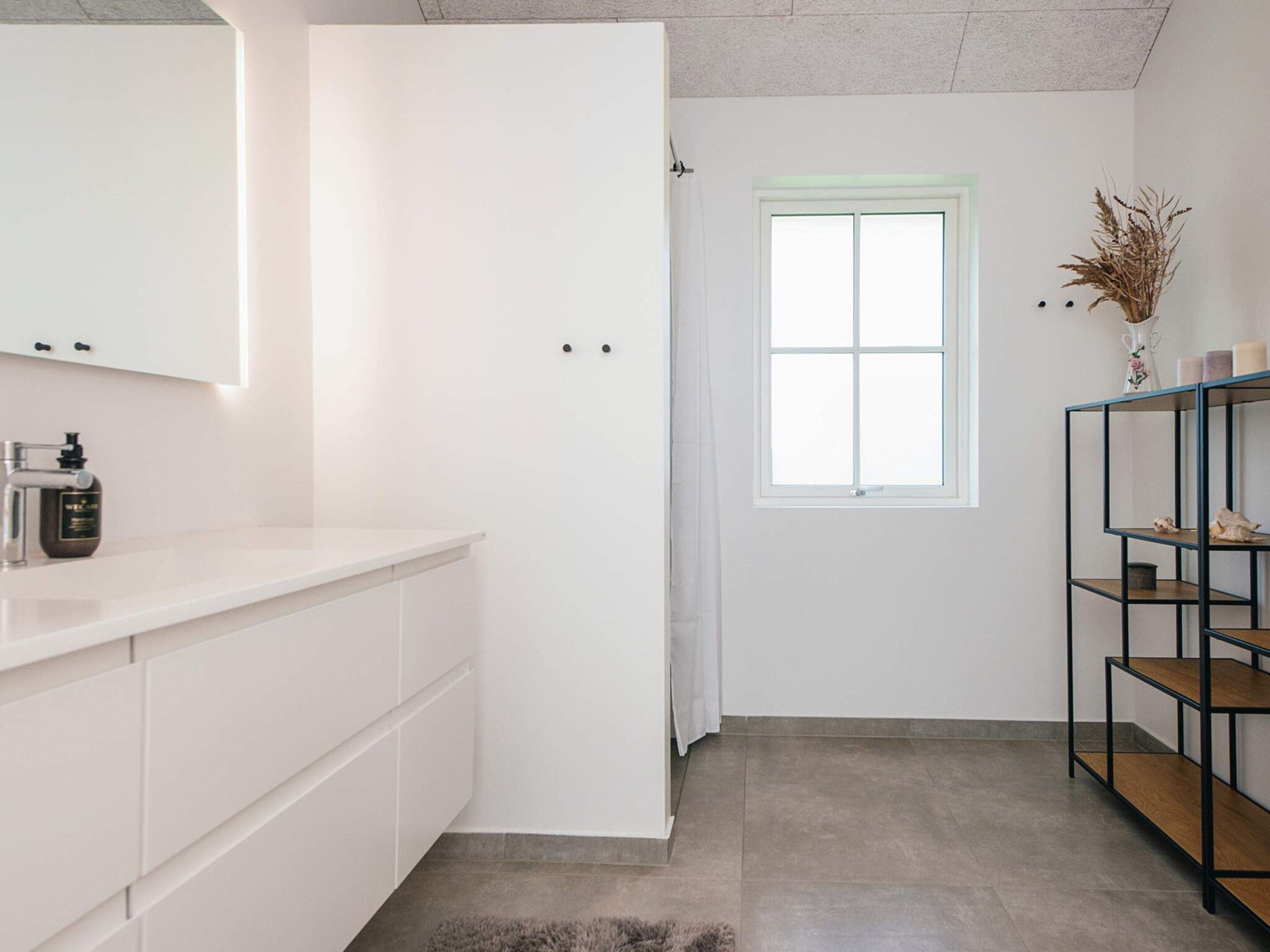 Casa de banho com toucador branco, espelho, frasco de sabonete e janela com vista para o exterior.