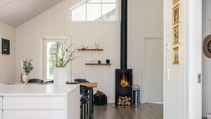 A modern interior with a central fireplace, wooden flooring, and a white wall with shelves. - 5 Star Holiday Home in Brovst (Brovst)