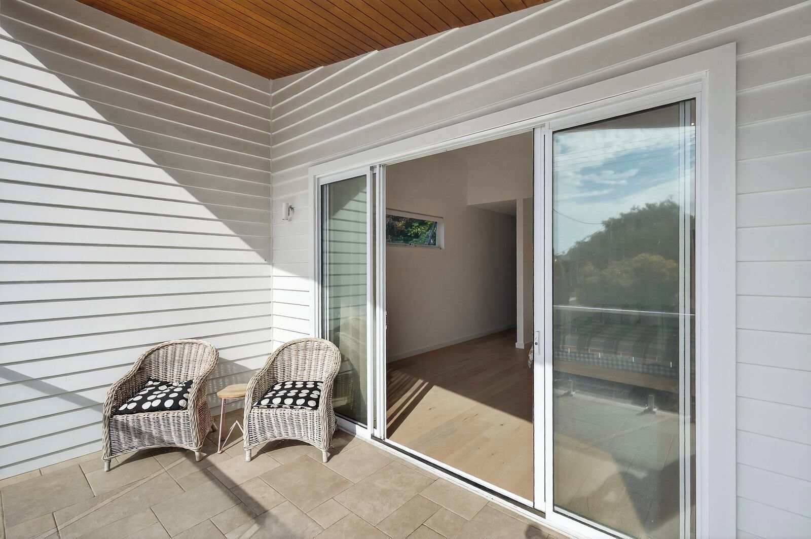 A balcony with two wicker chairs, a sliding glass door, and a view of the interior.