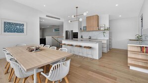 A modern kitchen with a central island, bar stools, and a dining area with a wooden table and white chairs. - 15A Charteris St, Port Elliot Walk to Horseshoe Bay (Port Elliot)