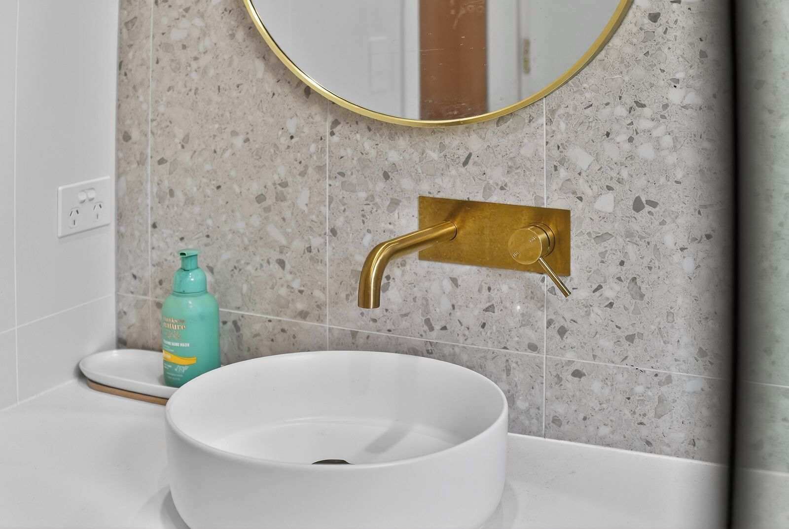 A bathroom with a white sink, a gold faucet, and a mirror with a gold frame.