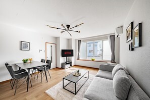 A modern living room with a dining area, a grey sofa, a coffee table, and a TV displaying 'NETFLIX'. - ASAHIKAWA STAY ECOLE 101  (Asahikawa)