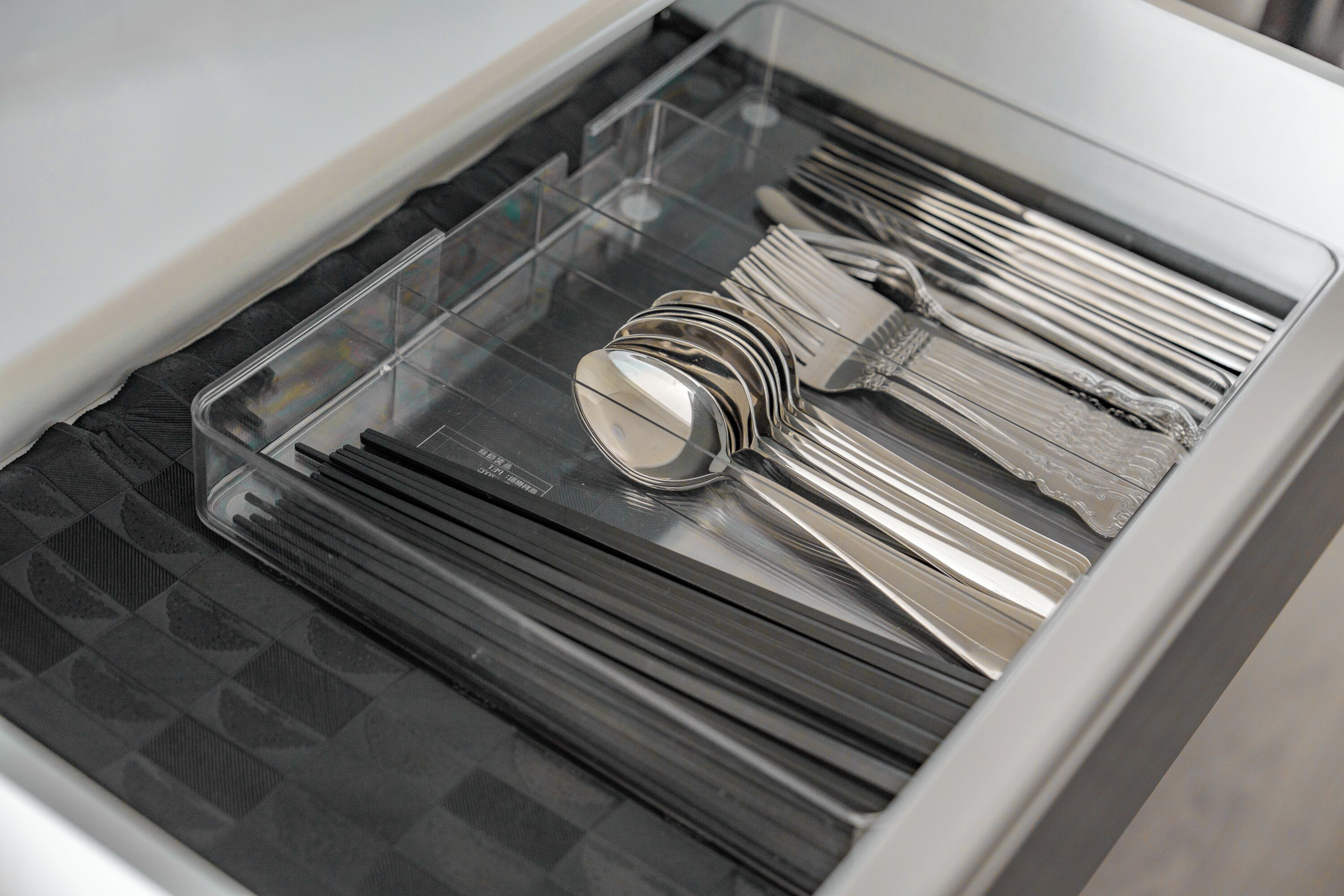 A drawer with neatly organized silverware and a transparent compartment.