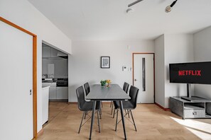 A modern dining area with a table and chairs, a kitchen in the background, and a TV displaying 'NETFLIX' on the wall. - ASAHIKAWA STAY ECOLE 101  (Asahikawa)
