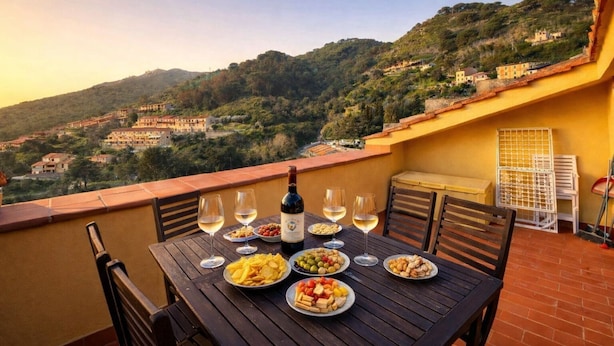A terrace with a table set for a meal, wine glasses, and a bottle of wine. - La Terrazza a Rio Elba (Rio dell'Elba)