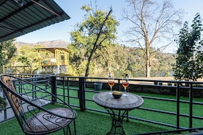 A patio with a table and chairs, a view of the landscape, and a building structure in the background. - ALAYA STAYS Lakefront Suite Naukuchiatal (Siloti Pant)