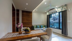 Un comedor moderno con una mesa de madera, sillas, un florero con flores y vistas al exterior a través de un ventanal grande.