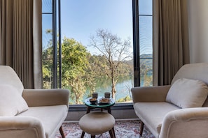 A room with two sofas facing a table with a bowl and two cups, a view of a lake and trees through large windows.
